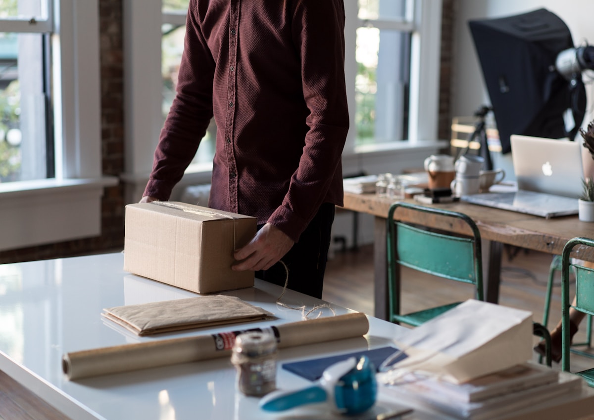 A person packing a cardboard box in a small workspace
